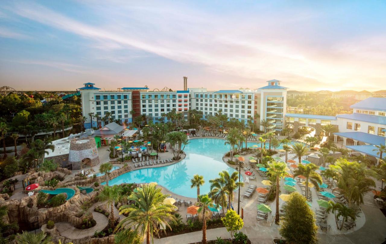 long curvy pool in front of a resort with waterpark in orlando, there are palm trees and lounge chairs with umbrellas near the pool at sunrise