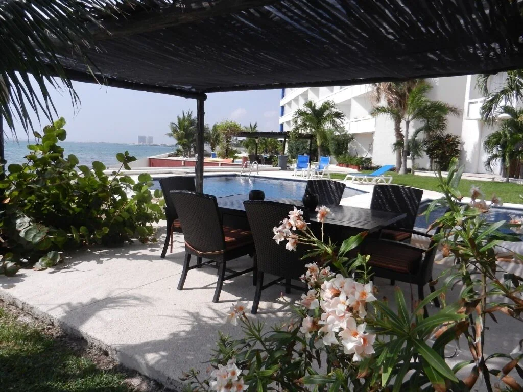 View of beautiful tropical flowers, a covered outdoor dining area, and the pool and ocean beyond at the Affordable Oceanfront