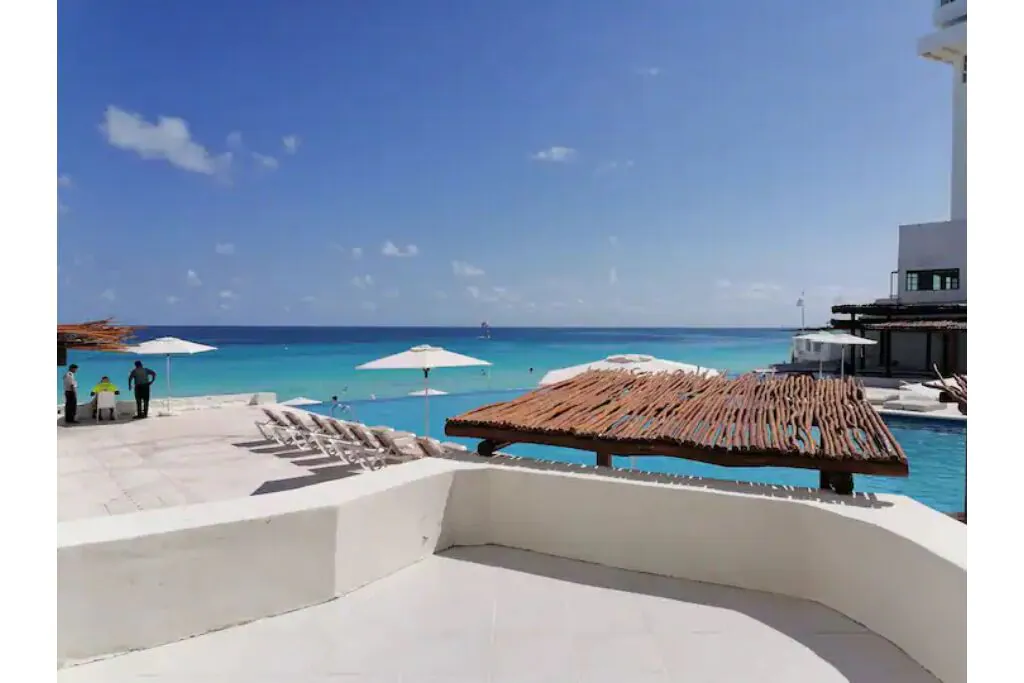 View of a luxurious pool area with an infinity pool, lots of umbrellas, and the turquoise waters beyond.  