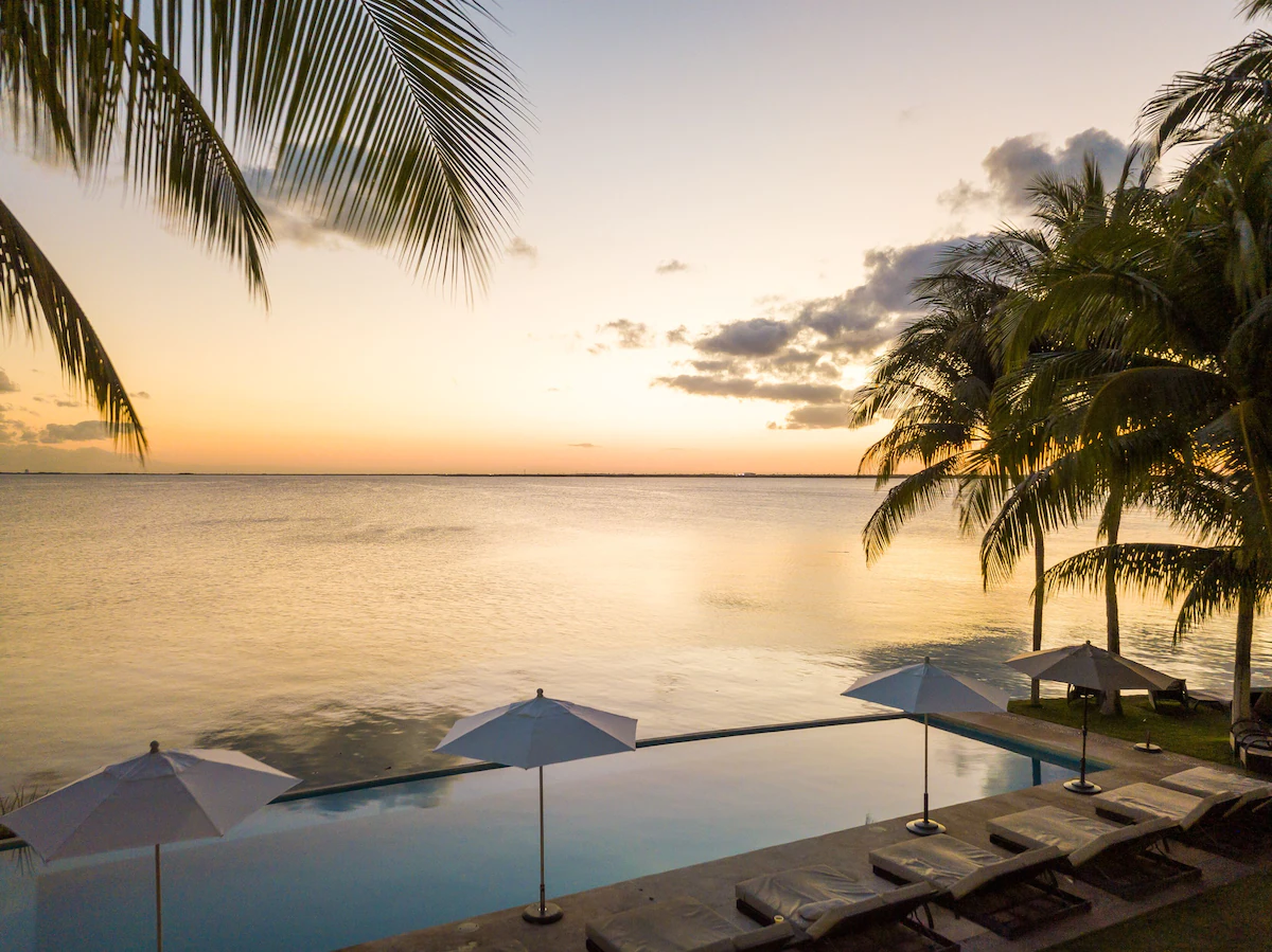 View of the beautiful infinity pool surrounded by lounge chairs and umbrellas. It overlooks the ocean beyond, which definitely makes this one of the best airbnbs in Cancun.