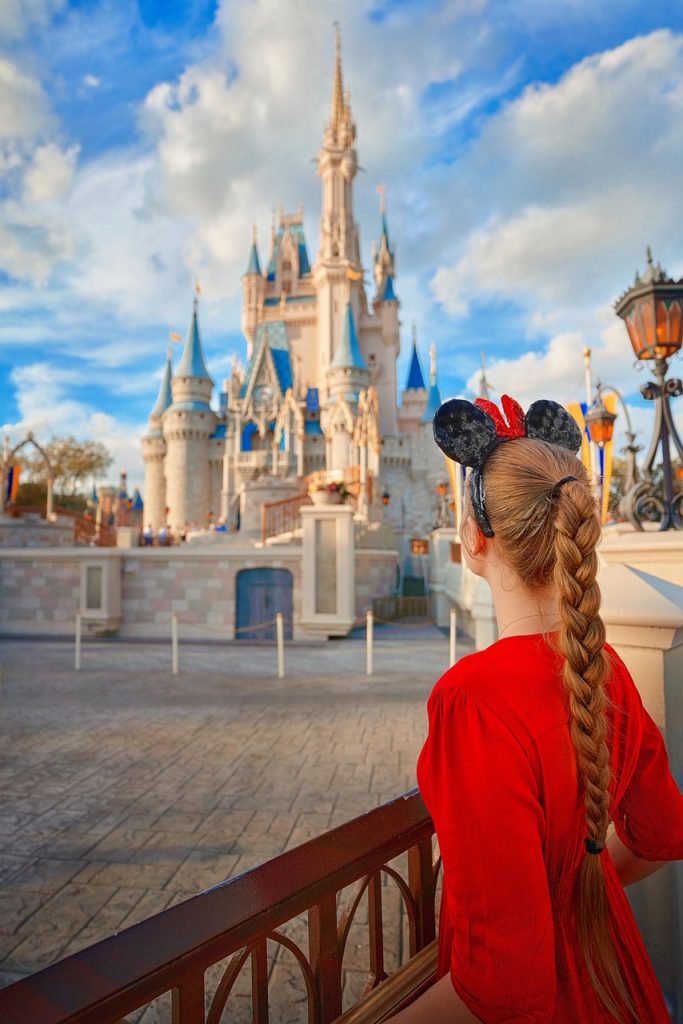 A woman wearing a red dress, and sequin Minnie Mouse ears looking at the Magic Kingdom castle in Walt Disney World best things to do in the usa