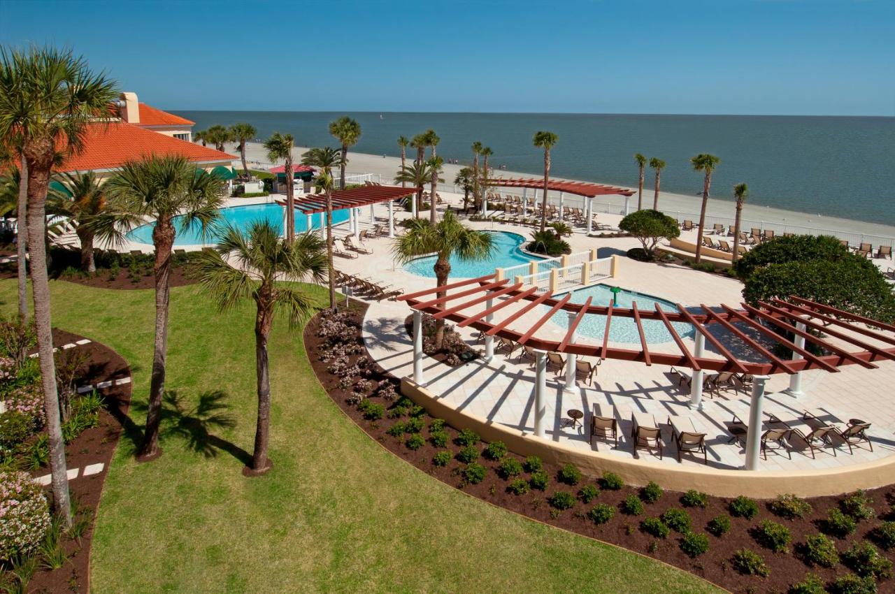 a grass and landscaped area with large palm trees and several pools boarding on a beach at one of the resorts in Georgia