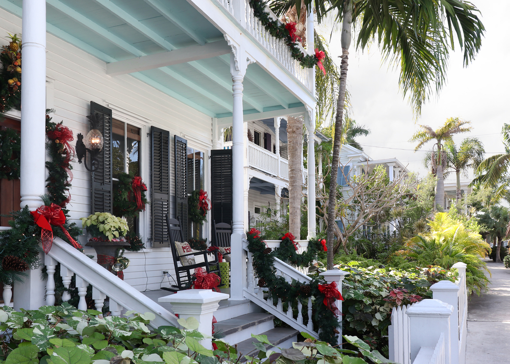Key West residence decorated for Christmas with wreaths, garland, and poinsettias and palm trees in the background. 