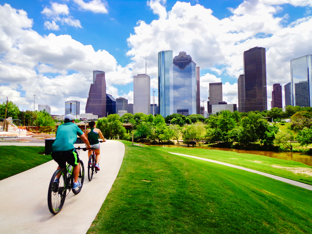 two people riding their bikes along a sidewalk down the bike trails in Houston Texas