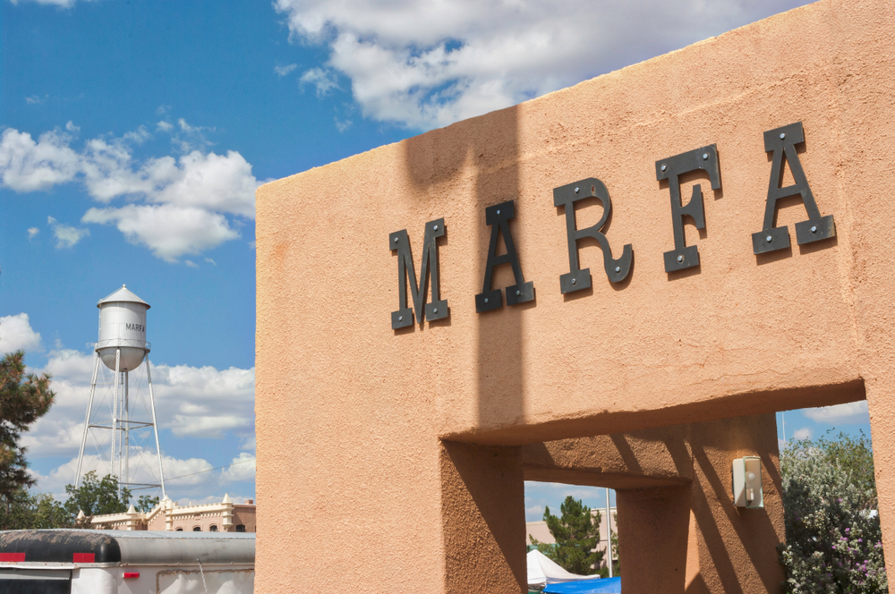 a brown building with the words Marfa in black letters and a water tower in the back round 