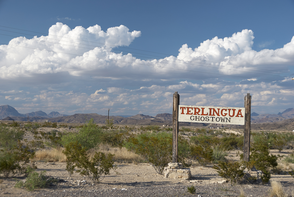 A sign in Terlingua texas that reads Terlingua Ghost Town. with big mountains in the back and white clouds in the sky. this is one of the. best weekend getaways in Texas