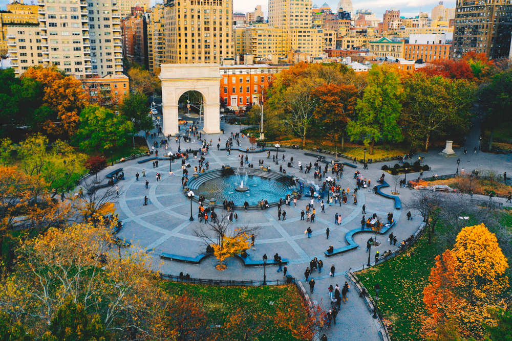 a photo of Washington Square Park in NYC during the fall the trees are beautiful shades or orange, red, and green. with the many skyscrapers in the back round