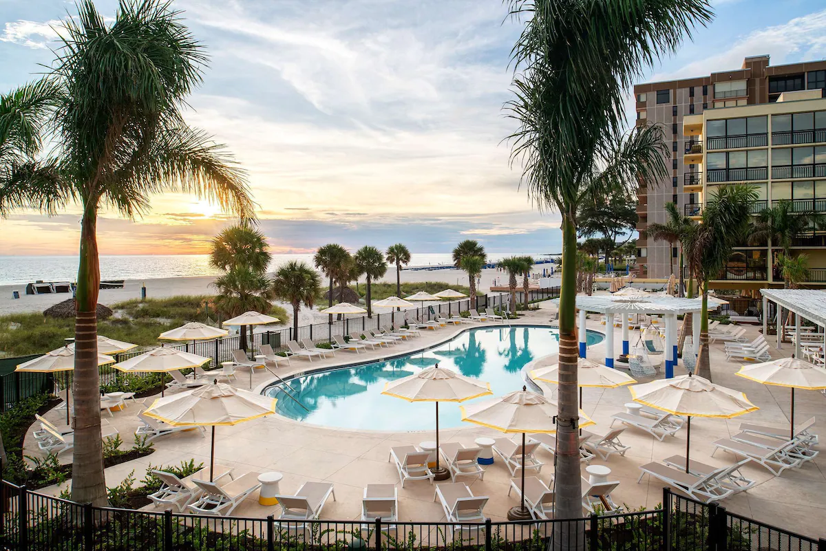 A stunning beachside pool at sunset shows private cabanas, easy beach access, palm trees, a bar and the nearby rooms at an all inclusive. 