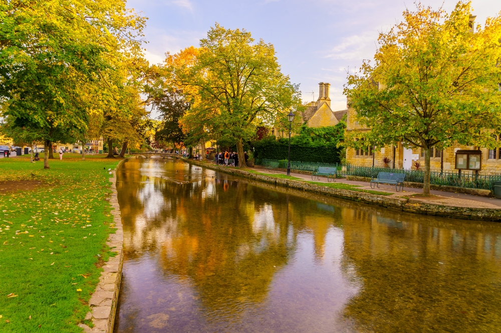 Sunset scene of typical houses, the river Windrush, locals and visitors, in the village Bourton-on-the-Water, the Cotswolds region, England, UK