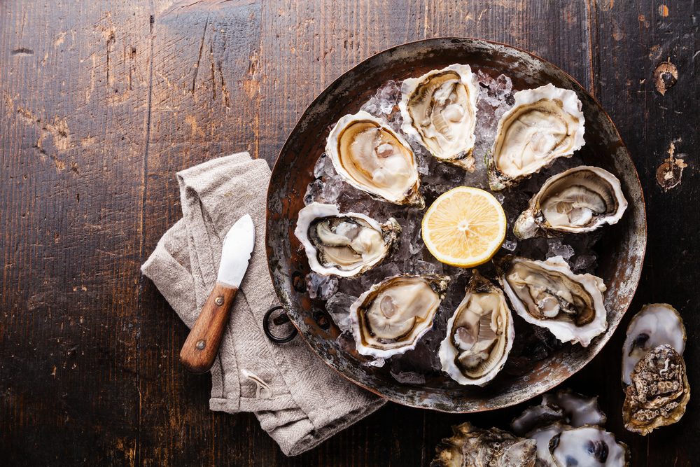 a wood table complete with a metal bowl filled with shucked oysters on ice!