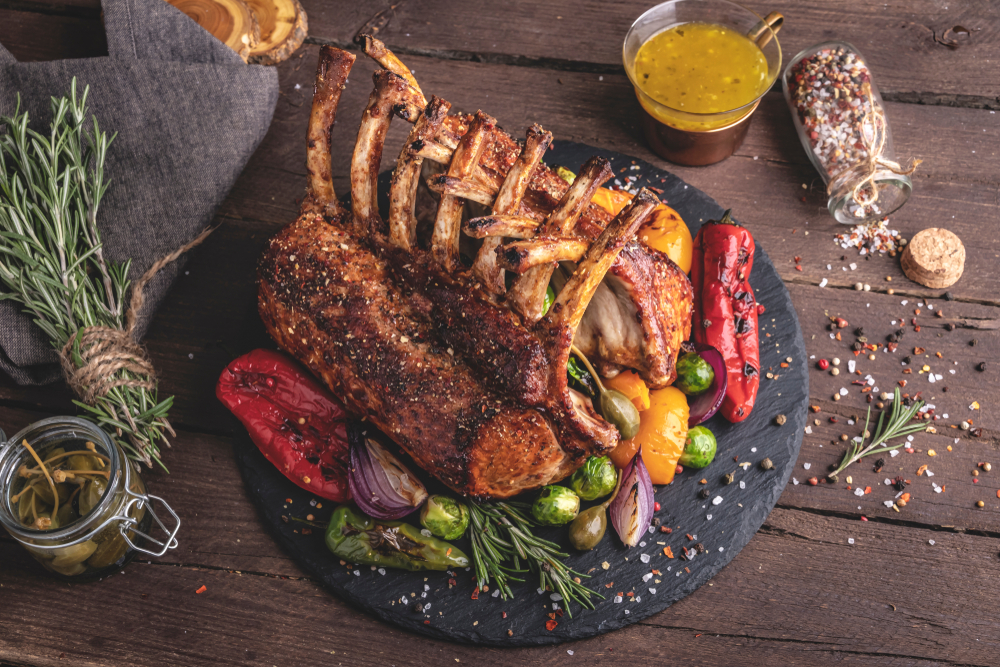 a slate circular platter with a rack of lamb, baked peppers, brussel sprouts, shallows and swigs of rosemary with plenty of spices for this twist on mexican dishes at this option for the best restaurants in san antonio!