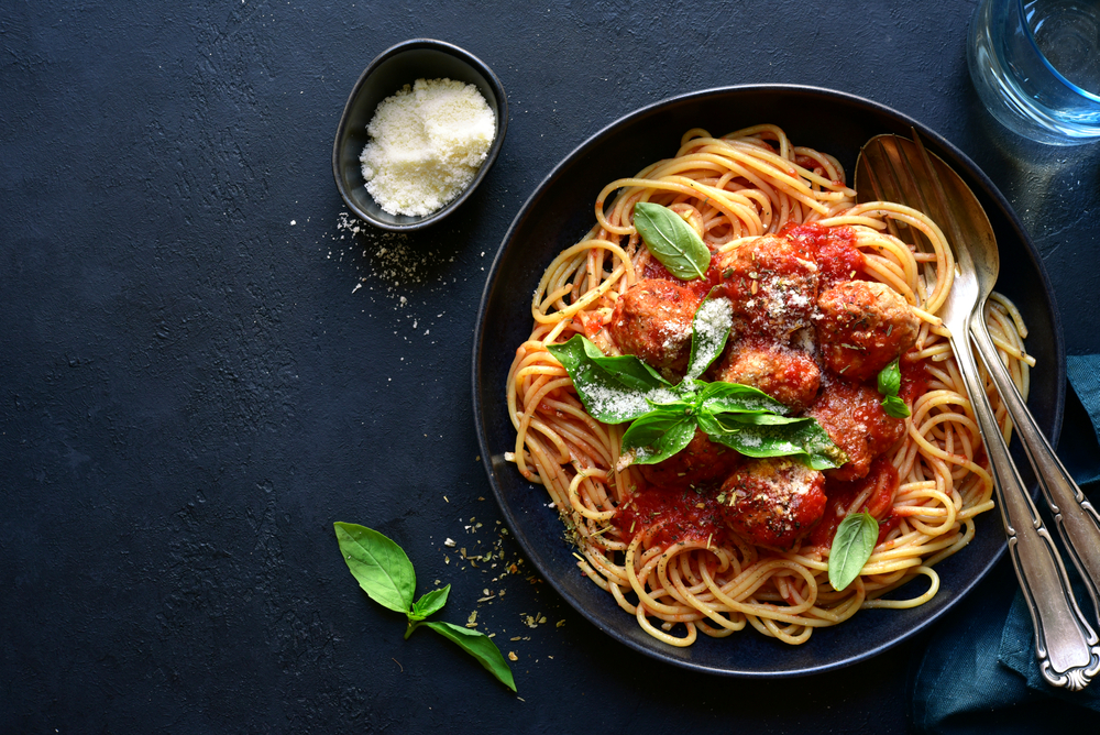 a dark blue bowl filled with spaghetti and meatballs topped with red sauce and basil leaves with a tiny bit of parmesan