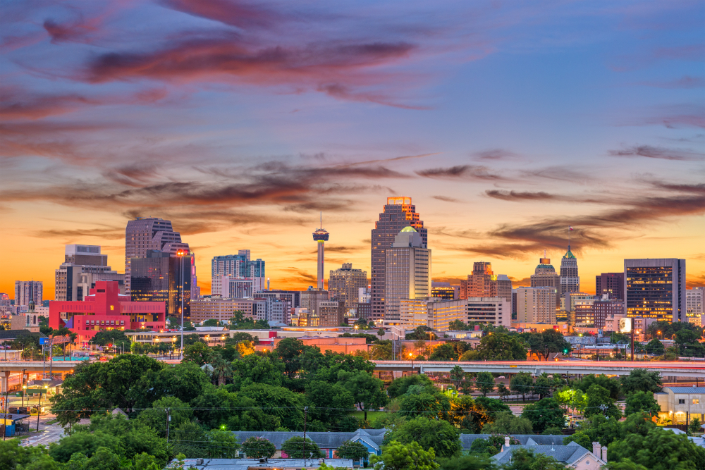 a beautiful dusky image of the san antonio skyline, with gorgeous green trees, tall skyliners and bright lights!