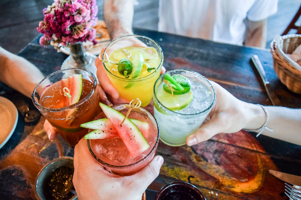 friends cheersing their glasses together over a rustic table with lovely purple flowers in a bud vase and having a great time!