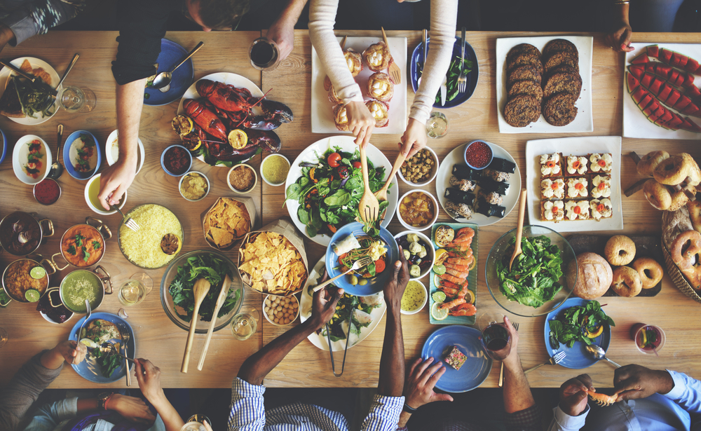 a lovely spread of food where people are taking their share with a large variety and plenty to choose from!