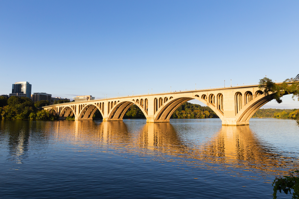 a beautiful image of the bridge over the potomac reflecting the sunset and reflecting onto a calm river from your view from the waterfront park!