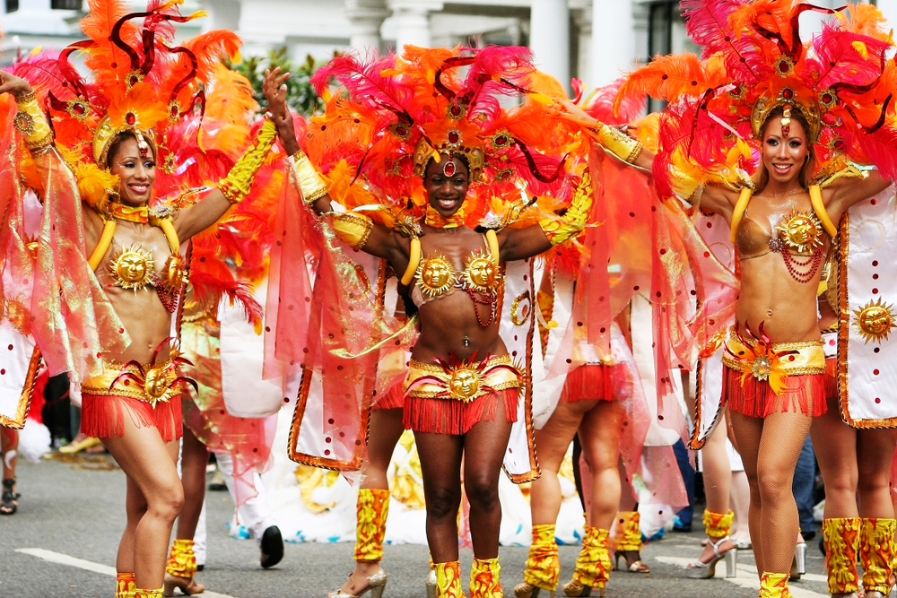Performers take part in the second day of Notting Hill Carnival. They are wearing orange and yellow costumns with orange feathers. 