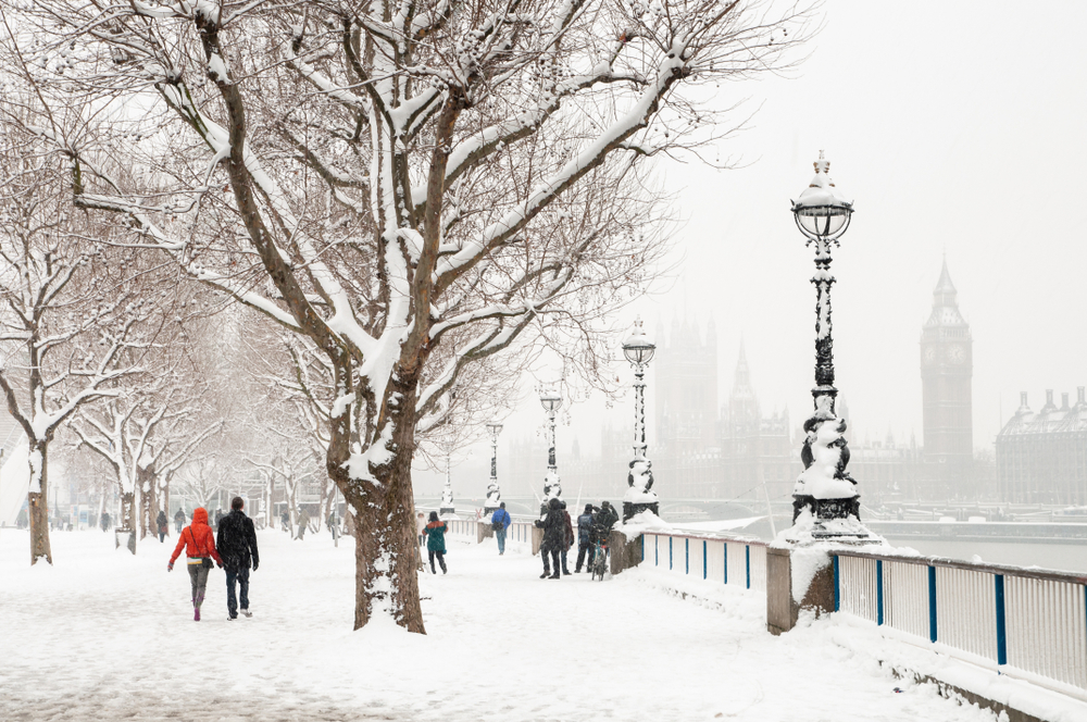 London snow scene during cold winter weather. The ground is covered in snow and you see across the river to Big Ben.  