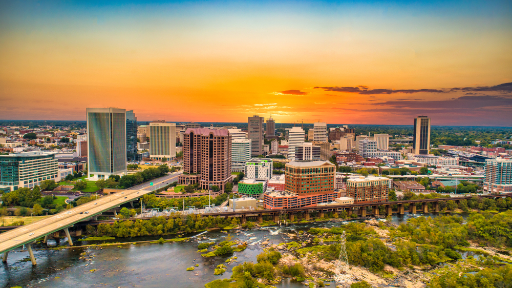 city with lots of buildings, a highway, a river with rapids, and a sunset with orange and yellow sky