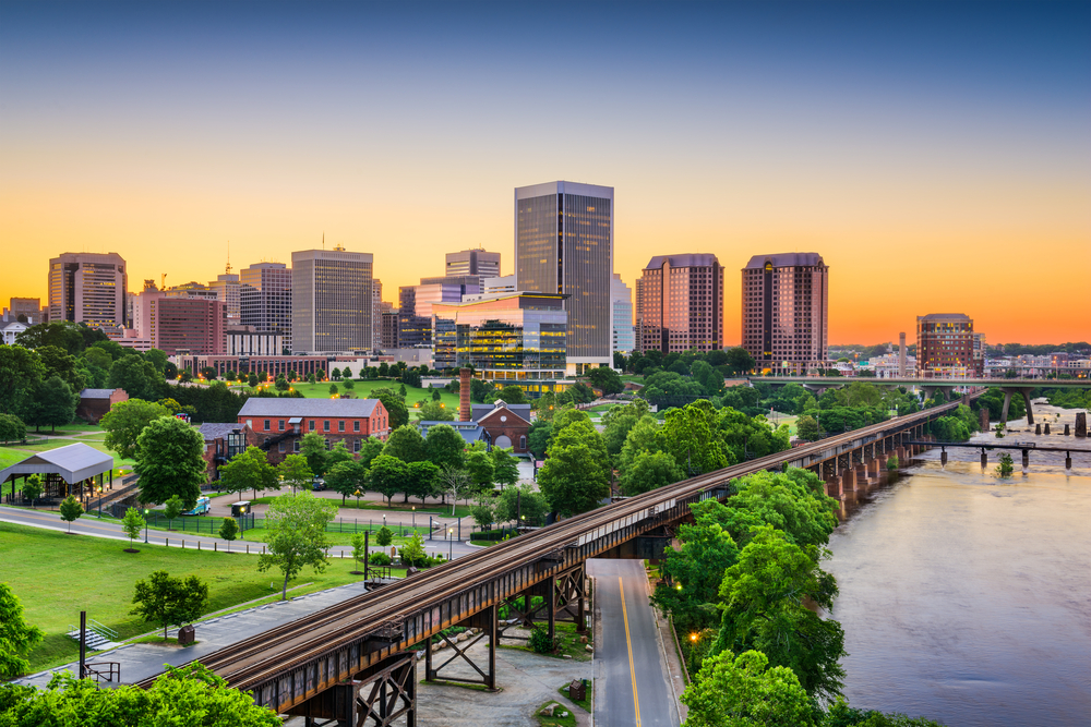 a beautiful view of the Alexandria town in Virginia with buildings and a railroad running through the center with a orange sunset in the sky and green trees