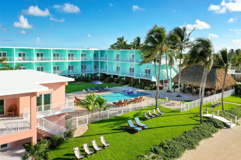 The view of a funky mid-century style hotel that is painted bright turquoise and pale peach with a pool and palm trees