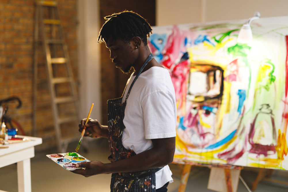 A man painting in a studio with a painting in the background