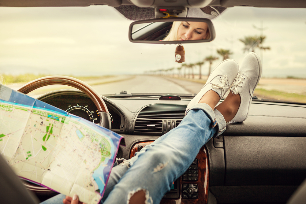 A woman with her feet on the dashboard looking at an attraction map on a road lined with palm trees