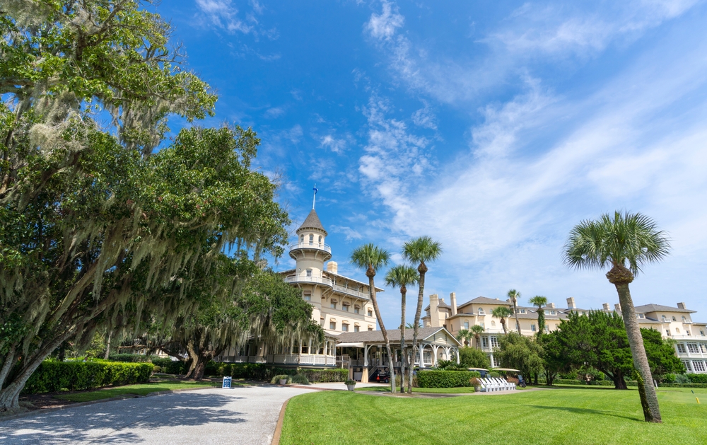 Famous moss-draped palm trees lining a sidewalk to a white building on a sunny day on Jekyll's Island, one of the best small towns in Georgia  