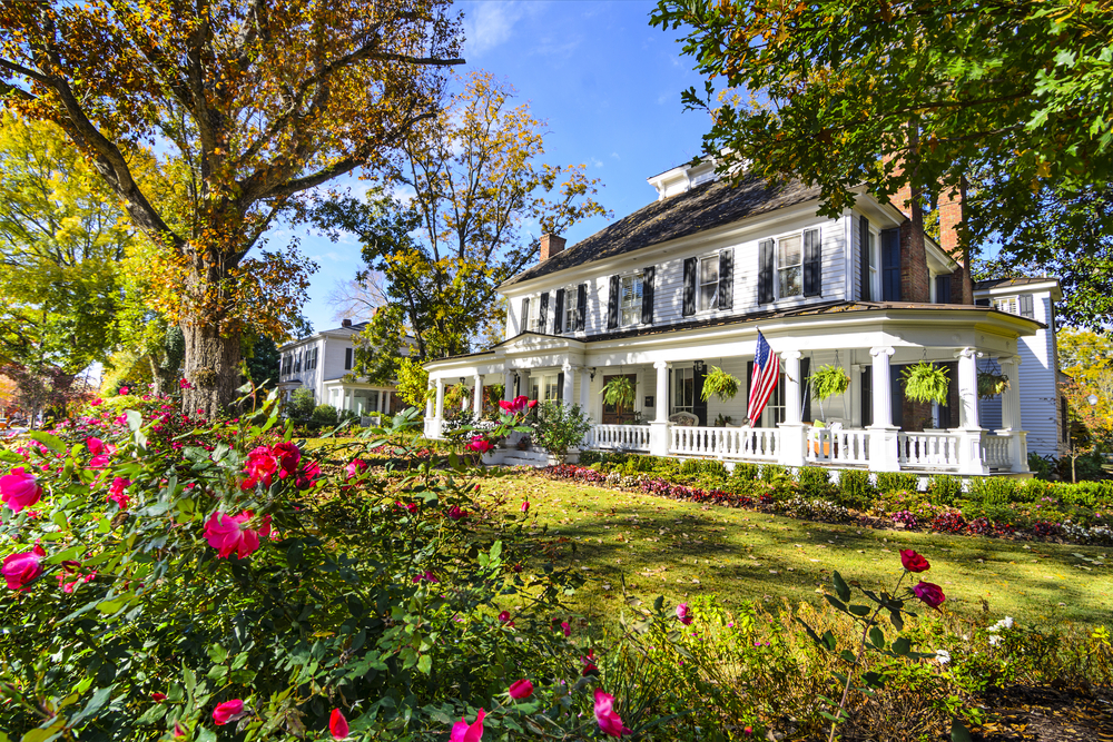 an old historical White House surrounded by greenery and pick flowers during the afternoon, what you will find walking through Madison, one of the best small towns in Georgia 