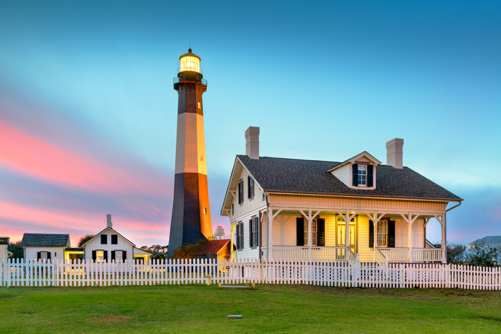 The Tybee Island lighthouse surrounded by white picket houses at dusk with green grass 