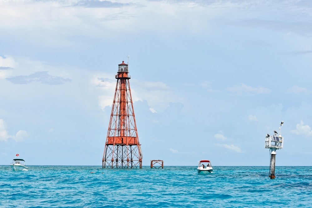 The Sombrero Key Light house in the ocean with two snorkeling boats nearby