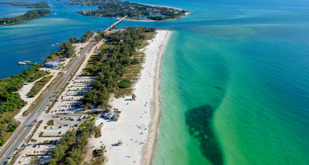 view of green and blue water with white sand beach from above on anna maria island