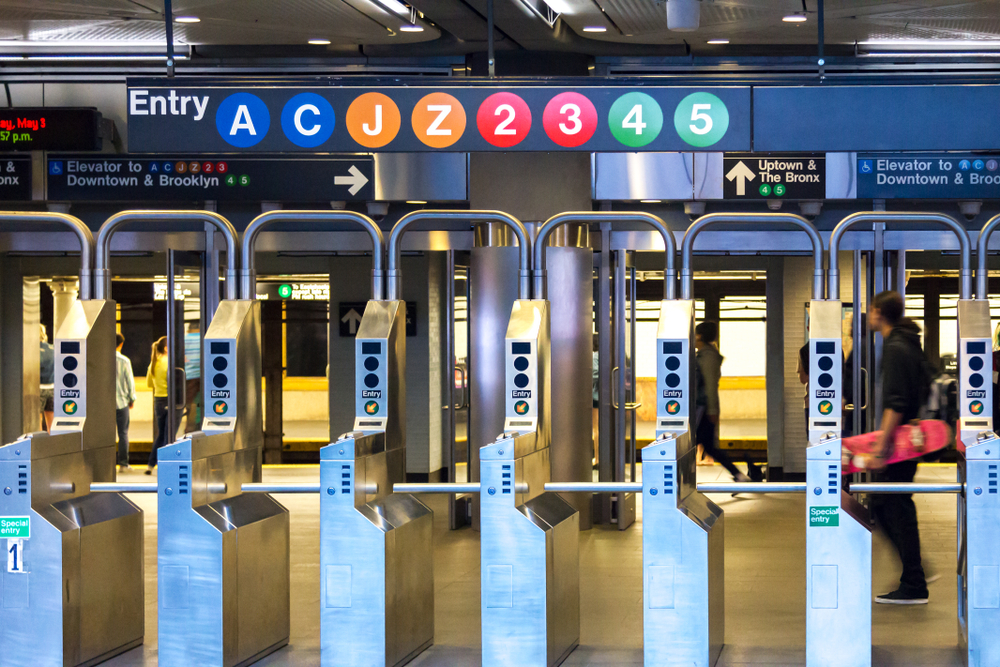 a view of the ticket taking machines in the center of the NY subway. you can see all the different lines to take and people walking by 