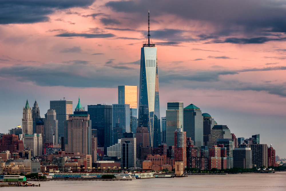 the view of the World Trade Center from New York during sunset. the clouds are pink and purple and the buildings have a reflection. this is a good stop for your weekend in NYC.