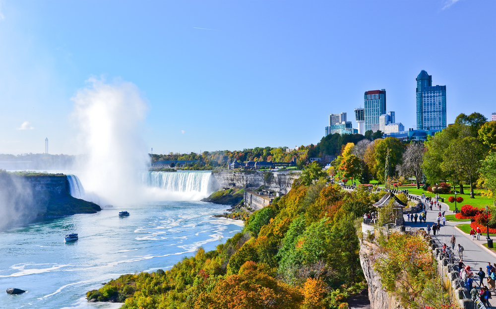 a beautiful image of bright, clear blue sky, a misty waterfall as well as bright and vibrant green leaves and grassy areas giving a great lookout towards this natural wonder!