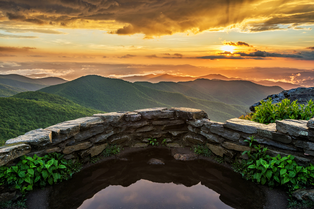 a rounded rock wall is on the edge of a mountain acting as an overlook of the mountains at sunset, best activity for a weekend in asheville
