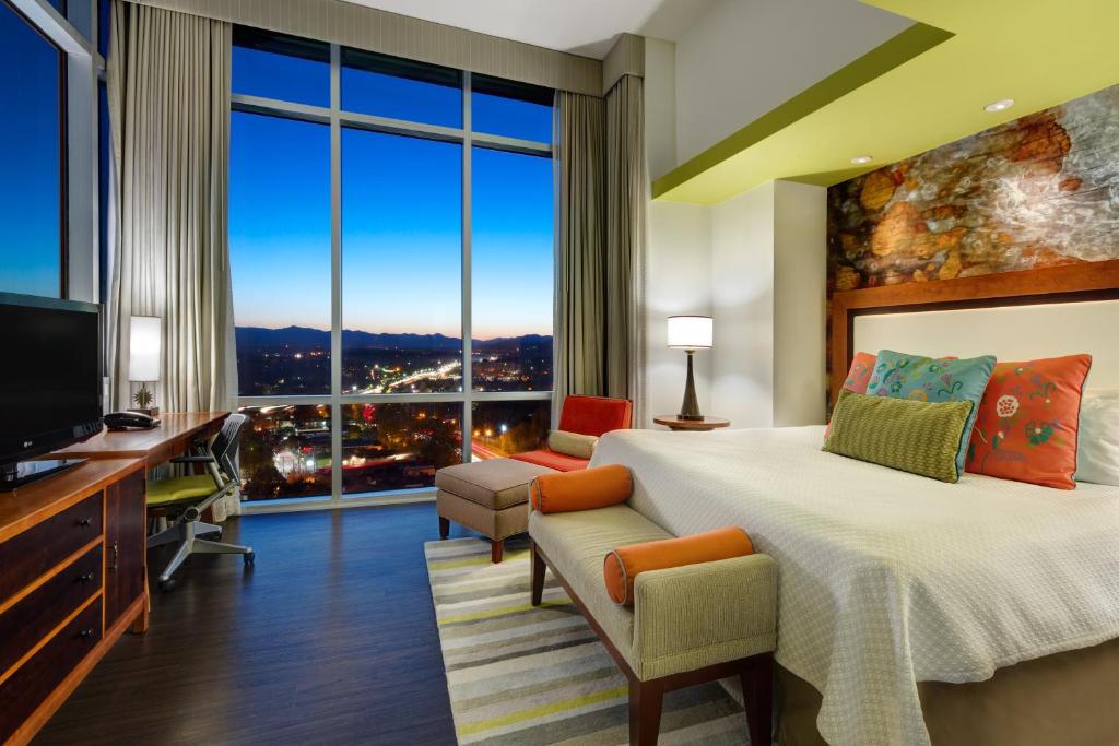 a hotel room wit a tv on the left and the bed on the right, large floor to ceiling windows are in the room overlooking the city