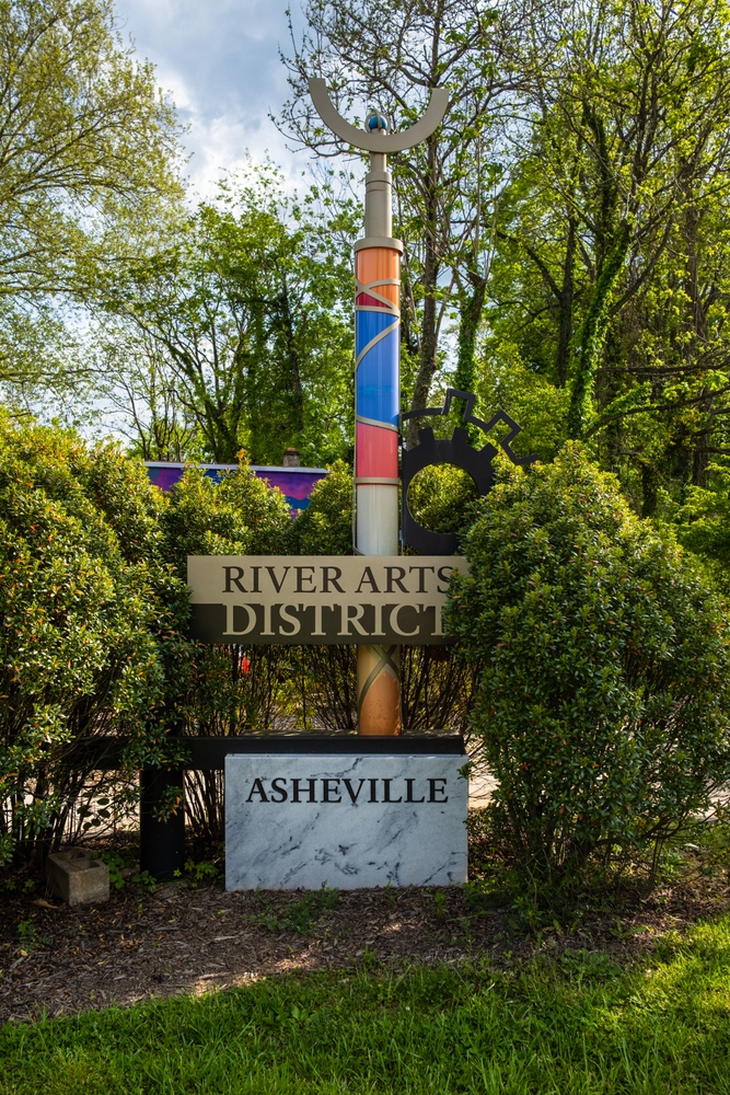 a pole amongst trees that is holding a sign that says river arts district asheville