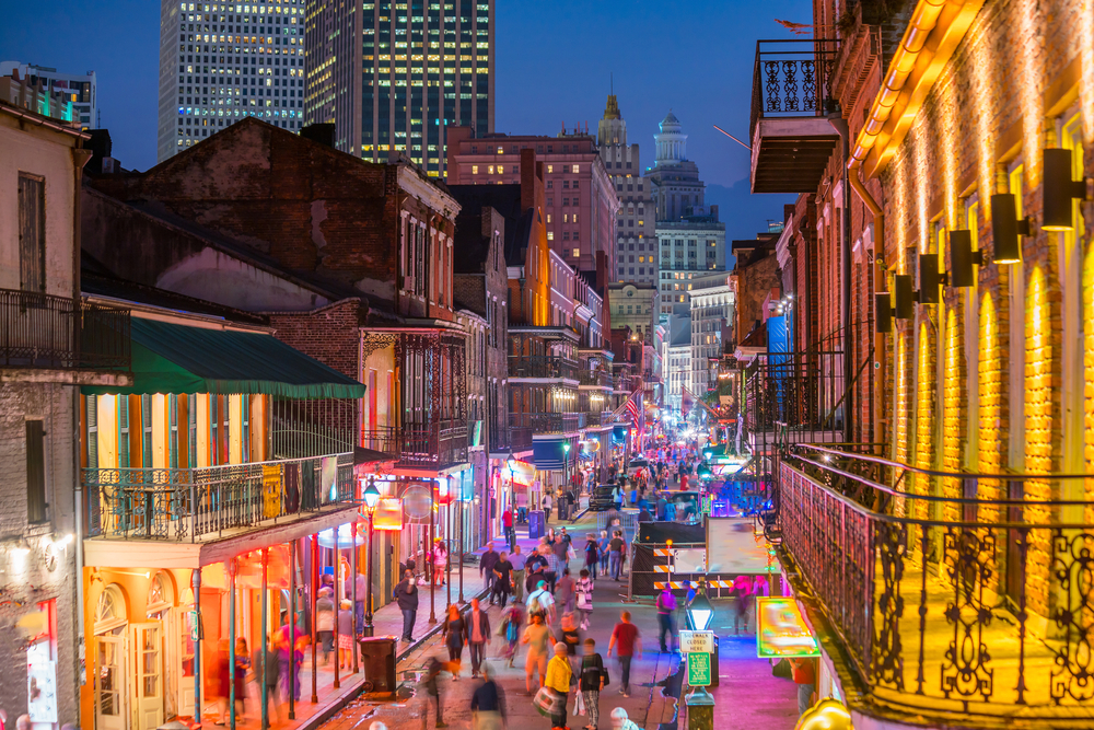 the neon lights from the bars on bourbon street with people walking down the street