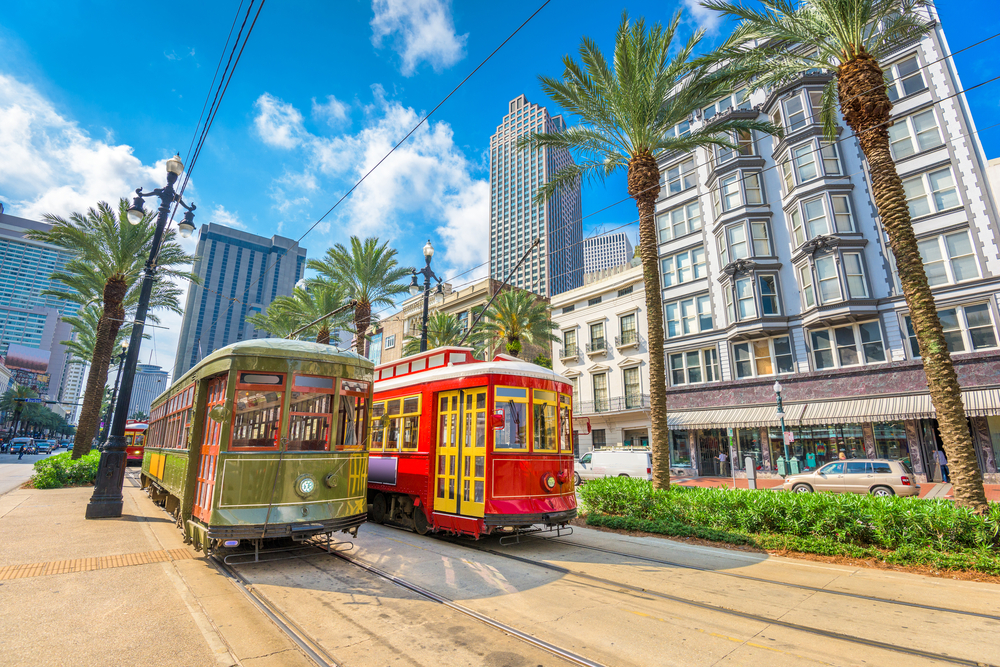 Two streetcars on the track in New Orleans surrounded by buildings and palm trees