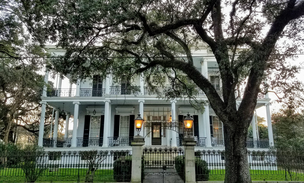 one of the mansion homes in the garden district with large oak tees and white columns on the front of ff a white house