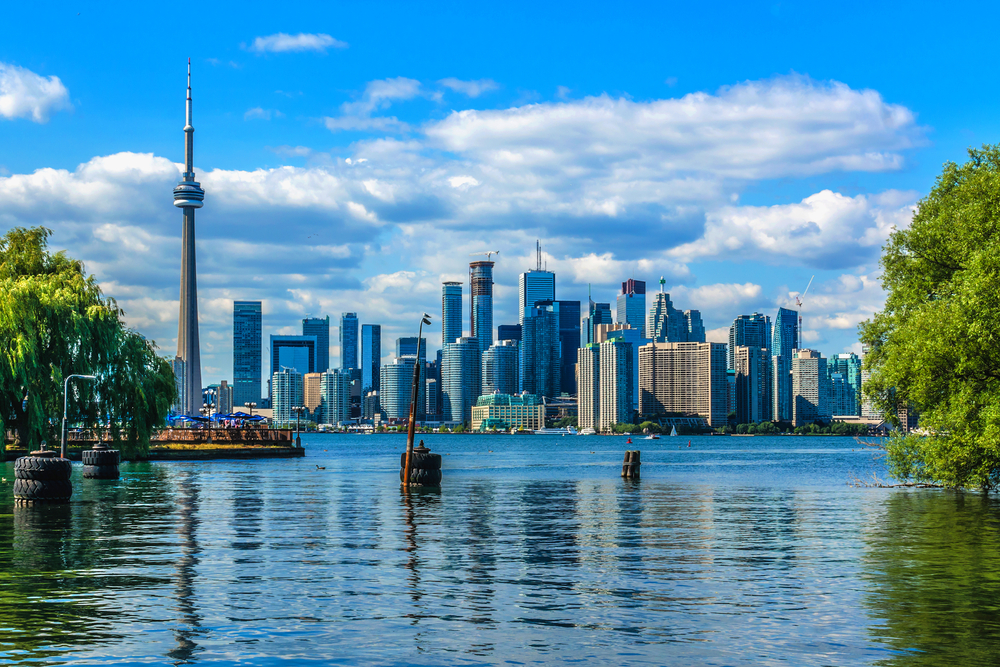 bright blue water and sky, vibrant green trees, on this image of lake ontario with a great view of the CN Tower, a great view you'll see on your weekend in Toronto