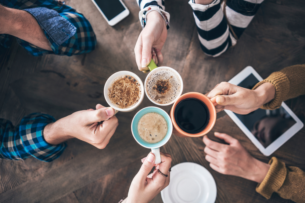 Coffee cups pulling together in the center, cheersing together over a table, perfect way to enjoy a morning on your weekend in Toronto