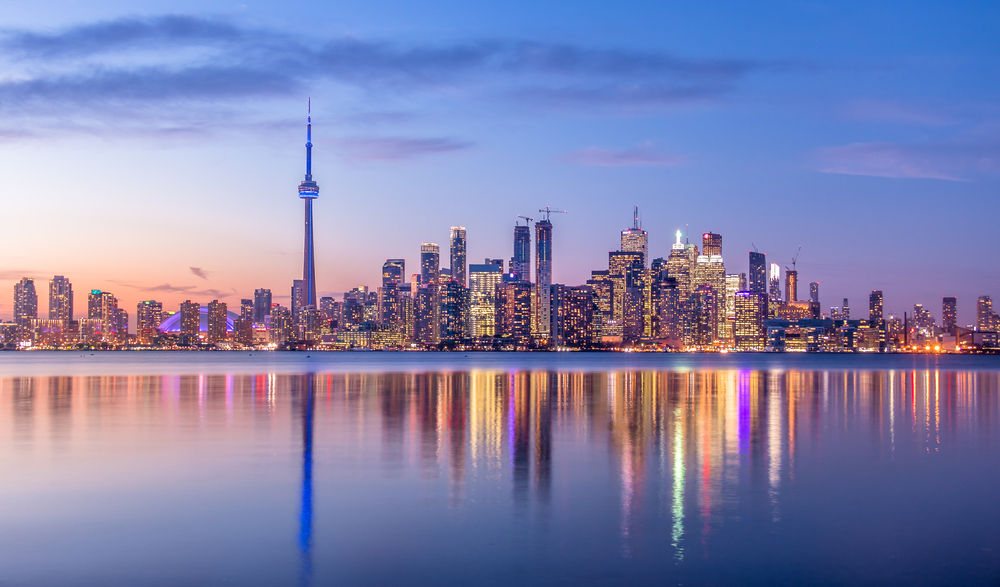 a dusky image of toronto's illuminated skyline, the lights reflecting in the water with a dusky pink and blue sky!
