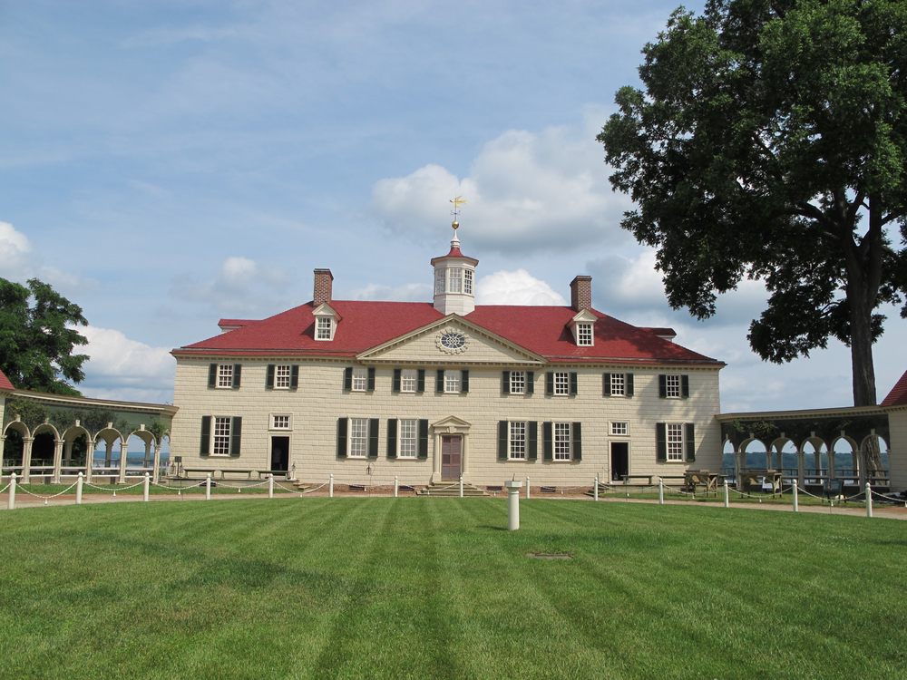 the view of mount Vernon from the garden. it is a big white home with a red roof and large green yard. 