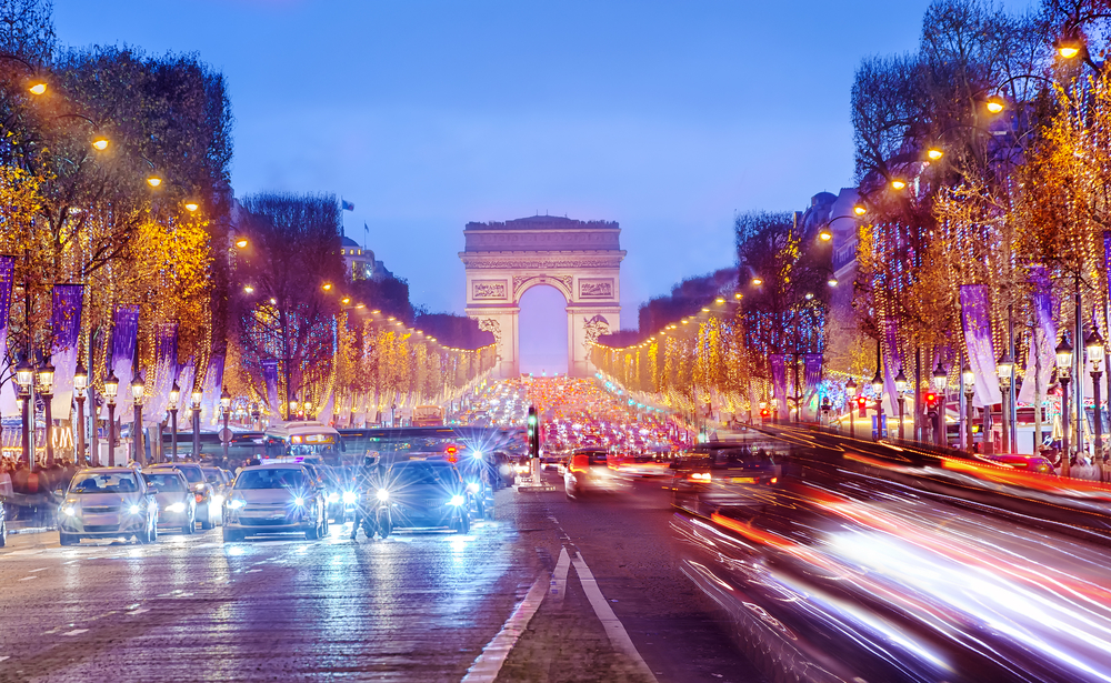 Dusk over the Champs-Elysées with many cars and rows of streetlights and trees.