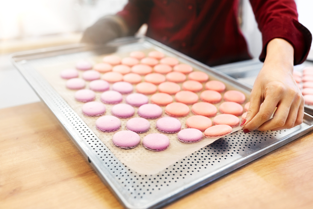 A person holding a pan of macaron cookies on parchment paper.