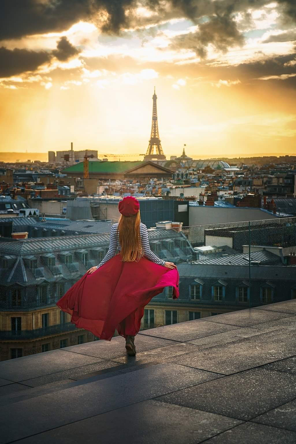 A sunset view on the viewing deck of Galleries Lafyette with the Eiffel Tower in the background with a girl looking on
