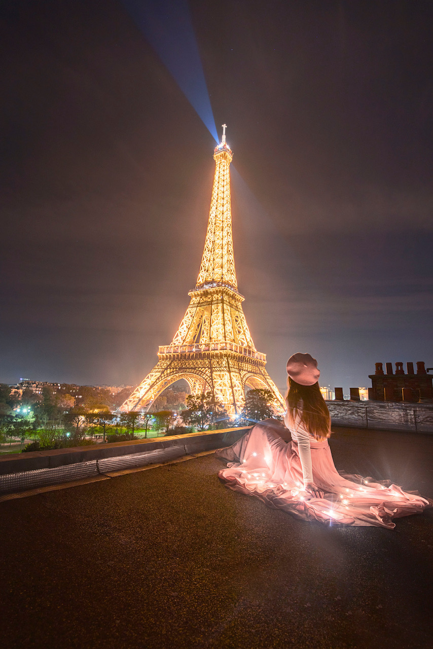 the eiffel tower light up at night with a girl on a rooftop watching it sparkle