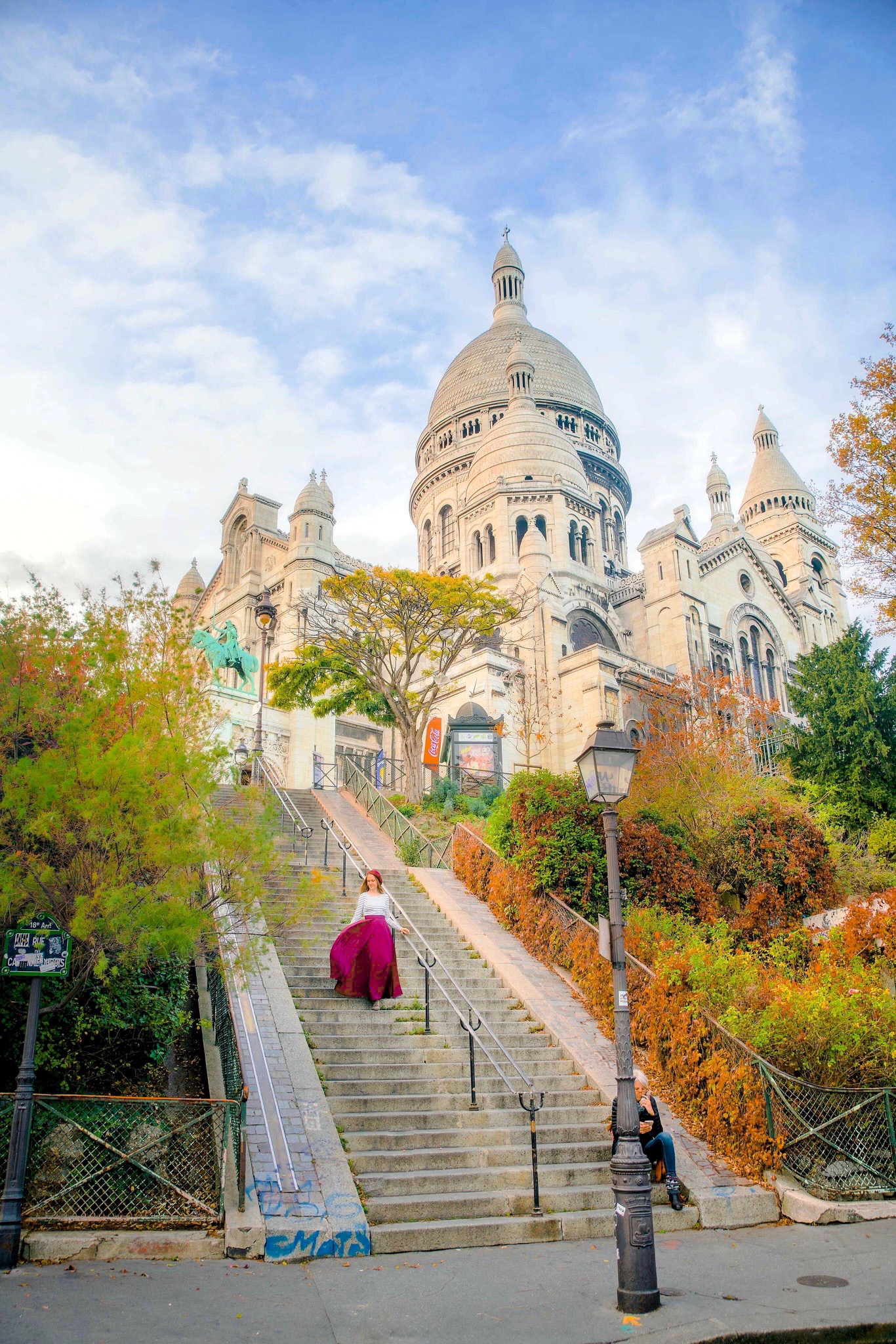 A girl in a Magenta skirt and Beret walking down the steps during fall with the Sacre Coeur in the background